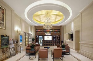 Un hall de hotel con candelabro, zona de estar, mostrador de recepción y una amplia estantería.