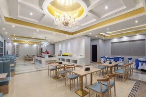 Ein geräumiger Hotel-Speiseraum mit mehreren Tischen und Stühlen, einer Bar in der Mitte und einem Kronleuchter.