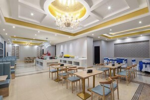 Amplia zona de comedor de hotel con numerosas mesas y sillas, un bar central y una araña.