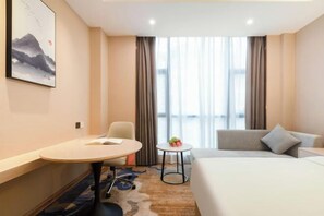 A hotel room with a bed, a desk, a chair, a small table with fruit, and a painting on the wall. - Vienna International Hotel (Du'an Station) (Du'an)
