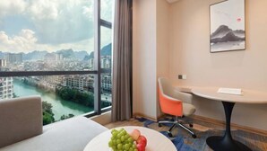 A hotel room with a large window, a desk, a chair, and a fruit bowl. - Vienna International Hotel (Du'an Station) (Du'an)