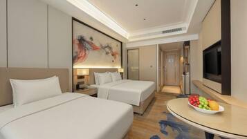 A hotel room with two beds, a flat-screen TV, a fruit bowl, and a painting on the wall.