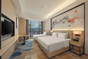 A hotel room with a large bed, a TV, a desk, and a view of the mountains.