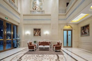 Un vestíbulo con techo alto, un área de estar central con alfombra estampada y una escalera que conduce a un nivel superior.