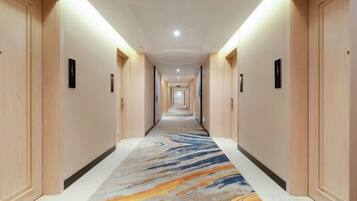 Un pasillo de hotel con puertas de madera, alfombra estampada de mármol e iluminación en el techo.