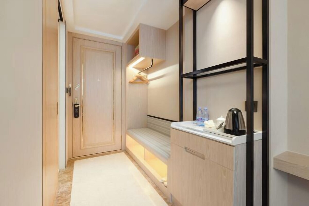 A narrow hallway with a door, a bench, a shelf with a kettle, and a small cabinet.