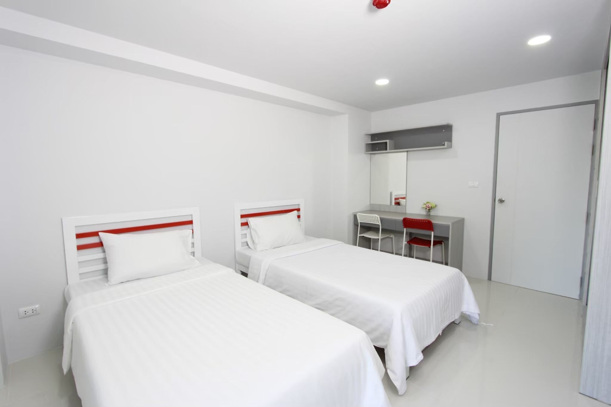 Quarto moderno e limpo com duas camas de solteiro, uma escrivaninha, uma cadeira e um guarda-roupa.