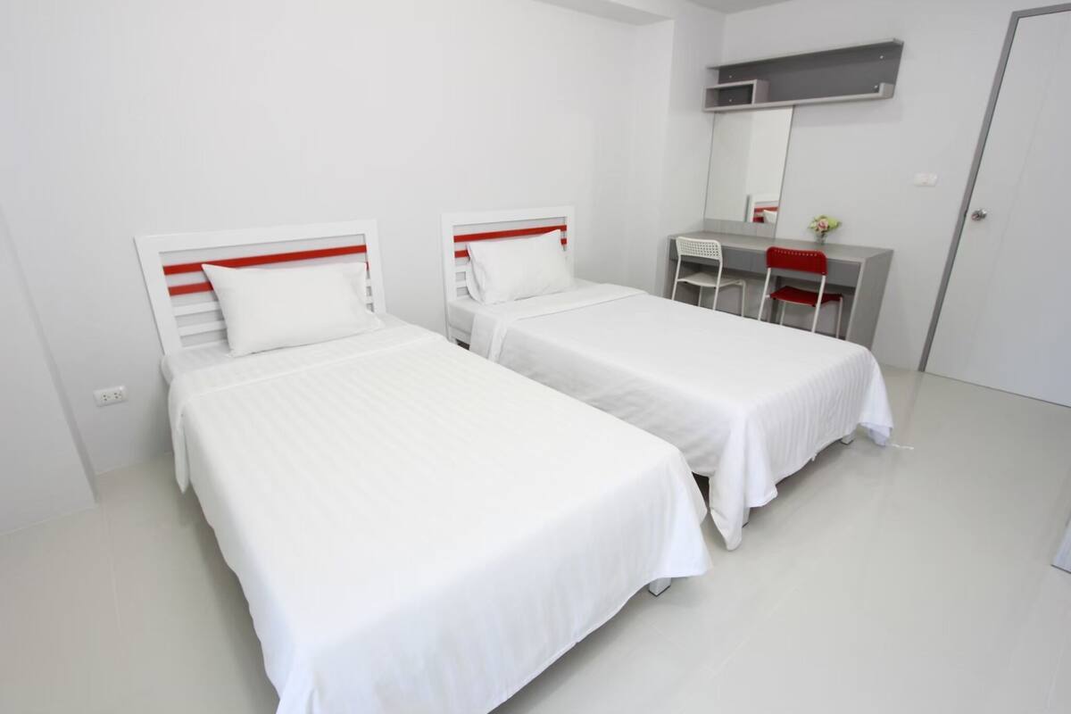 A clean, modern room with two single beds, a desk with a chair, and a mirror above the desk.