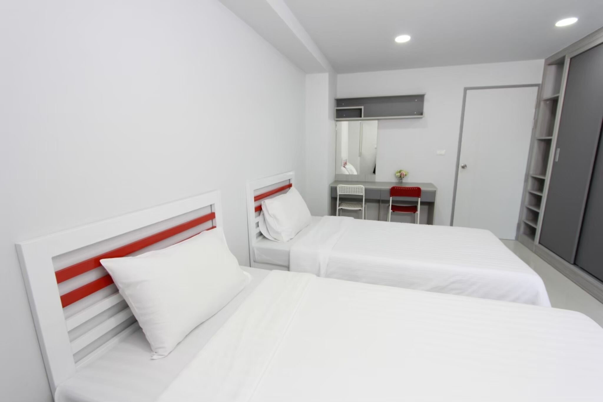 A modern hotel room with two beds, a vanity with a mirror, and a wardrobe.