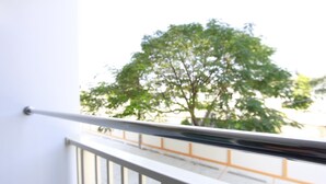 Un balcone con ringhiera in metallo, un muro bianco e un albero sullo sfondo.