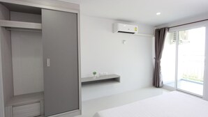 Una camera d'hotel con un letto grande, un armadio, un piccolo ripiano con una pianta, un condizionatore d'aria e una porta scorrevole in vetro che dà all'esterno.