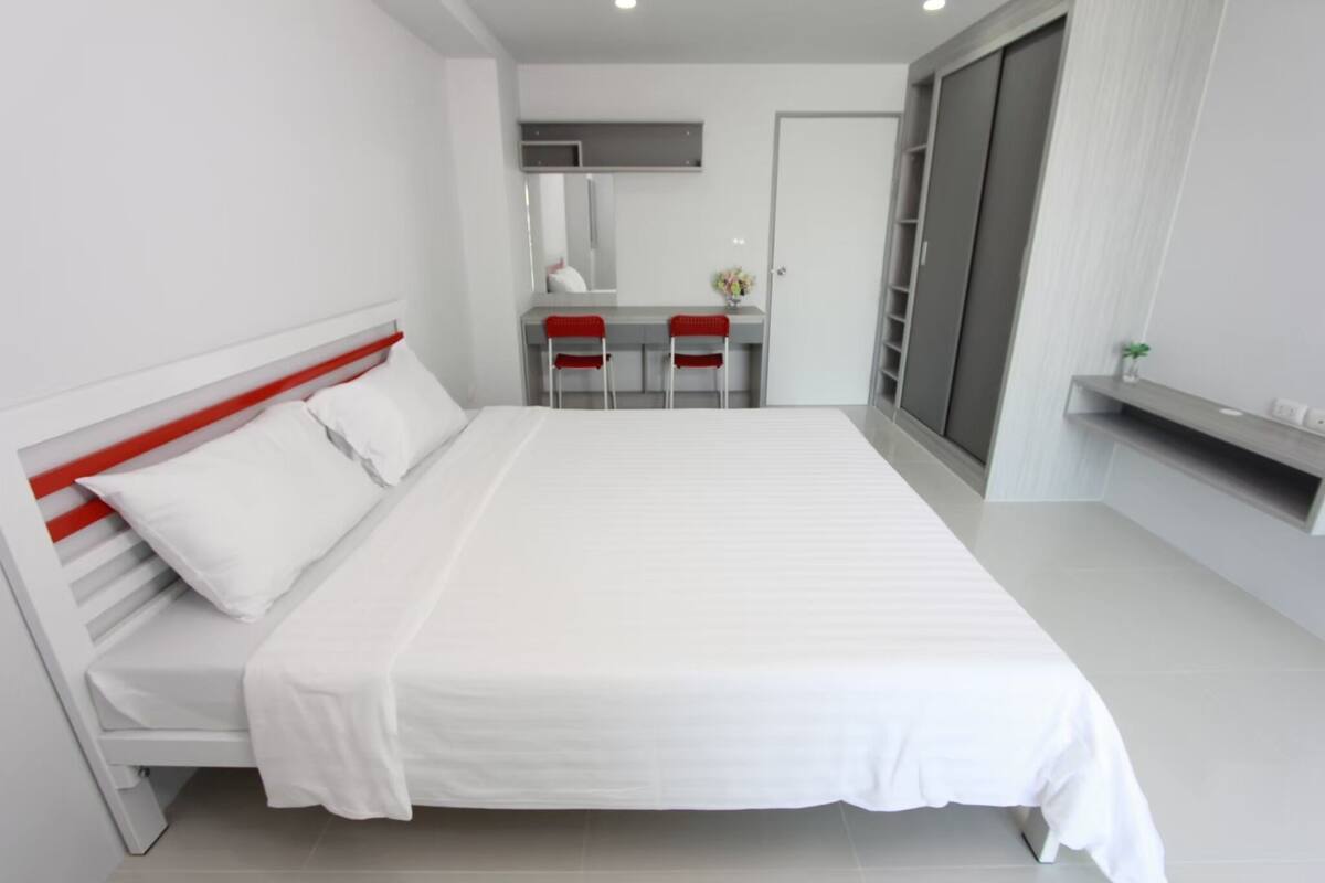 A modern bedroom with a large bed, a desk with two chairs, and a wardrobe.