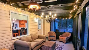 An enclosed porch with a sofa, two wicker chairs, a patterned rug, and string lights. - Auburn Tiger Alumni Retreat on 20 acres (Salem)
