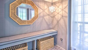 A room with a wooden wall, a mirrored octagonal frame, a hanging star-shaped light fixture, a striped bench, and wicker baskets. - 'The River Cottage' Isle of Wight Retreat w/ Dock (Midway)