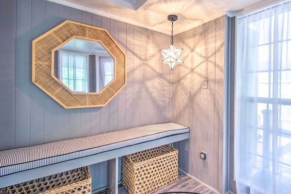 Una habitación con pared de madera, un marco octogonal con espejo, un lámpara en forma de estrella colgante, un banco a rayas y cestas de mimbre.
