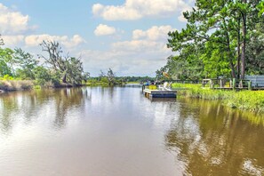 Un río tranquilo con un embarcadero y sillas a la derecha, rodeado de árboles y vegetación.
