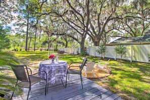 A deck with a table and chairs, surrounded by a lush garden and large trees. - 'The River Cottage' Isle of Wight Retreat w/ Dock (Midway)