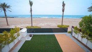 A patio with artificial grass, a seating area, and a view of the beach and ocean. - Eagle Hills (Al-Fujairah)