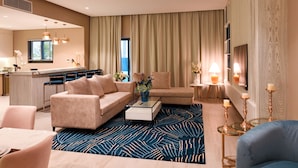 A modern hotel room with a sofa, armchair, coffee table, and a dining area with chairs and a table. - Eagle Hills (Al-Fujairah)