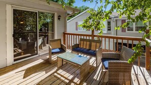 Une terrasse en bois, agrémentée de meubles en osier, notamment d’un canapé et de fauteuils, ainsi que d’une table avec un plateau en verre.