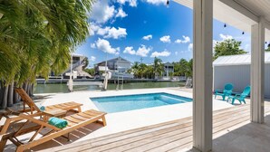 A pool area with wooden loungers and a view of a marina. - Lake It Easy: Relax in This Beautiful 3BR Canal Front Home on Summerland Key, Dockage & Dog-Friendly (Summerland Key)