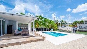 A covered outdoor area with a pool, wooden deck, and lounge chairs. - Lake It Easy: Relax in This Beautiful 3BR Canal Front Home on Summerland Key, Dockage & Dog-Friendly (Summerland Key)