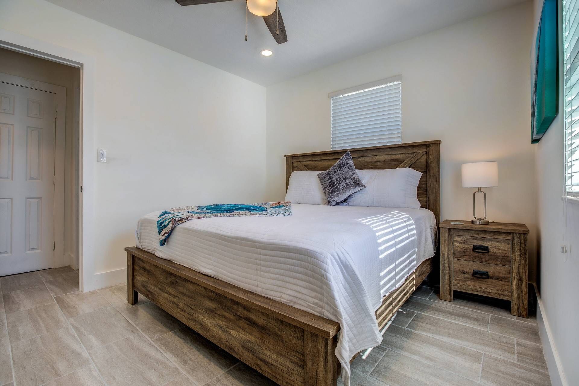 A bedroom with a wooden bed, a nightstand with a lamp, and a window with blinds.