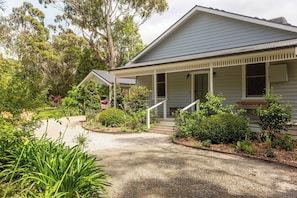 A two-story house with a porch, surrounded by a garden with various plants and trees.