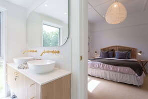 A modern bathroom with two sinks and a large mirror, and a bedroom with a bed and bedside table. - Luxury Villas Balnarring Botanical Cottage (Heated Pool) (Balnarring)