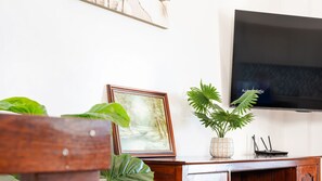 Ein Wohnzimmer mit Couchtisch aus Holz, einem gerahmten Bild, einer Topfpflanze, einem Flachbildfernseher und einem Router auf einer Holzeinrichtung.