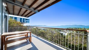 Ein Balkon mit einer hölzernen Bank, einem Metallgeländer und Blick auf eine Küstenlandschaft mit Bergen.