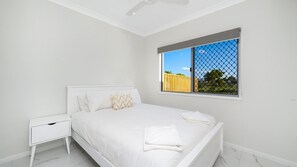 A bedroom with a bed, nightstand, and a window with a view of a fence and trees.