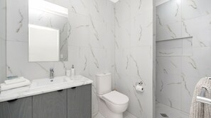 Ein Badezimmer mit Marmorwand, Waschbecken mit Spiegel, Toilette und Handtuchhalter.