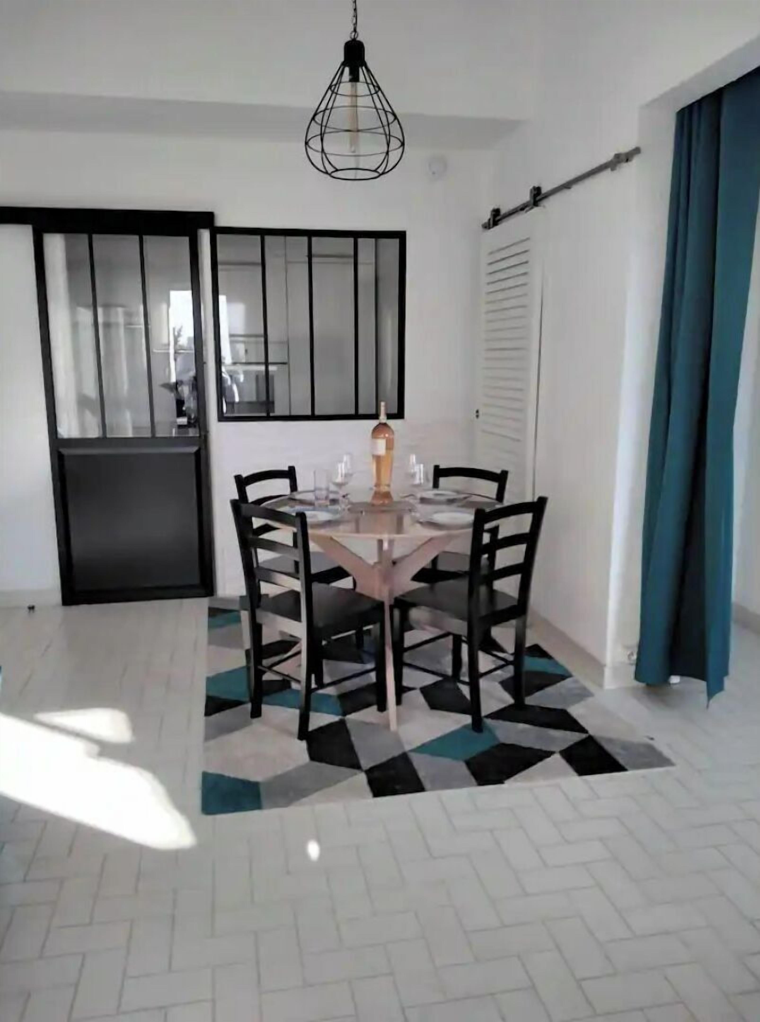A dining area with a round table, four chairs, a hanging light fixture, and a patterned rug.