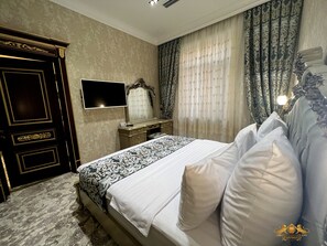 A bedroom with a large bed, a dresser, a vanity with a mirror, and a television on the wall.