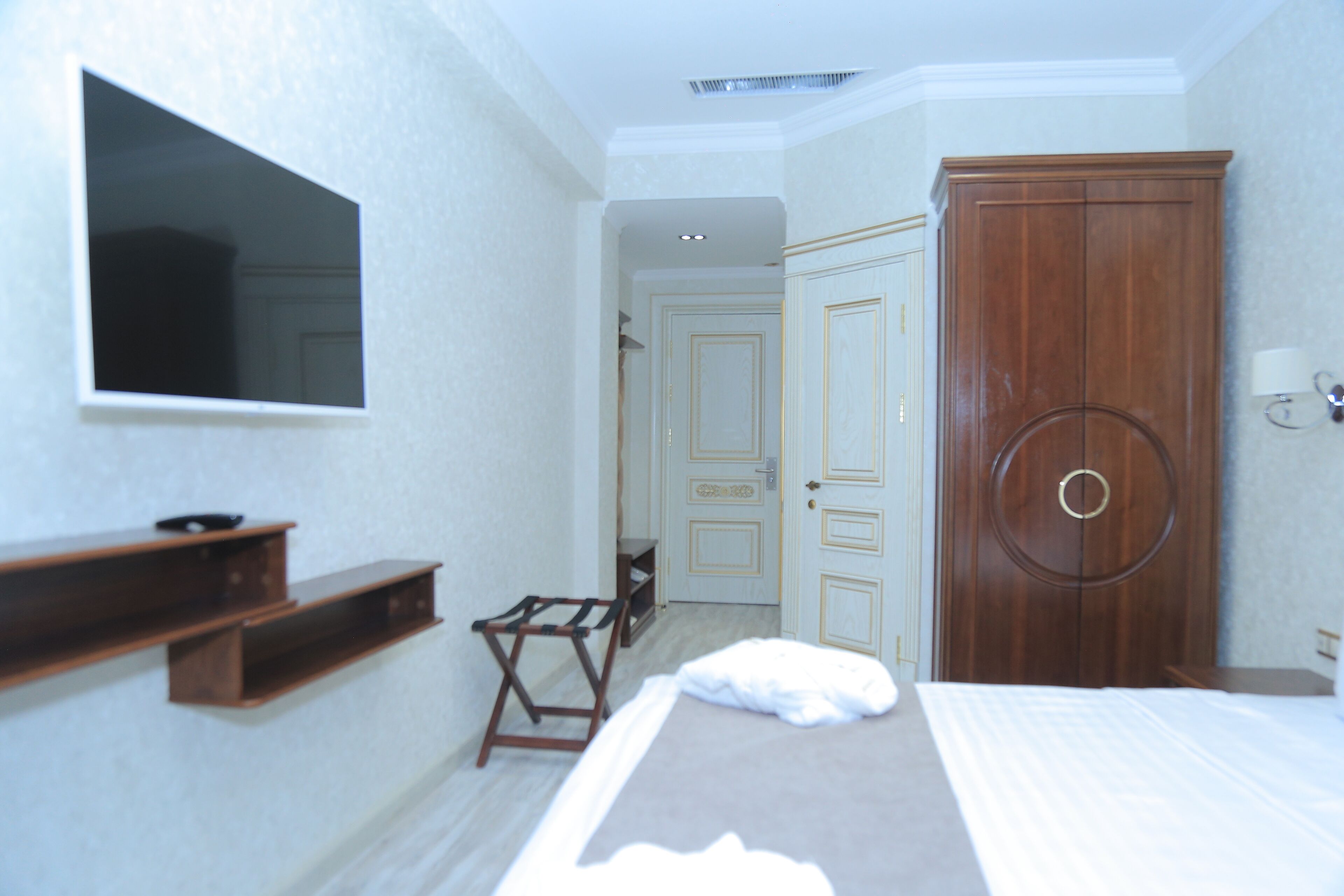 A hotel room with a bed, a TV mounted on the wall, a wardrobe, and a small table.