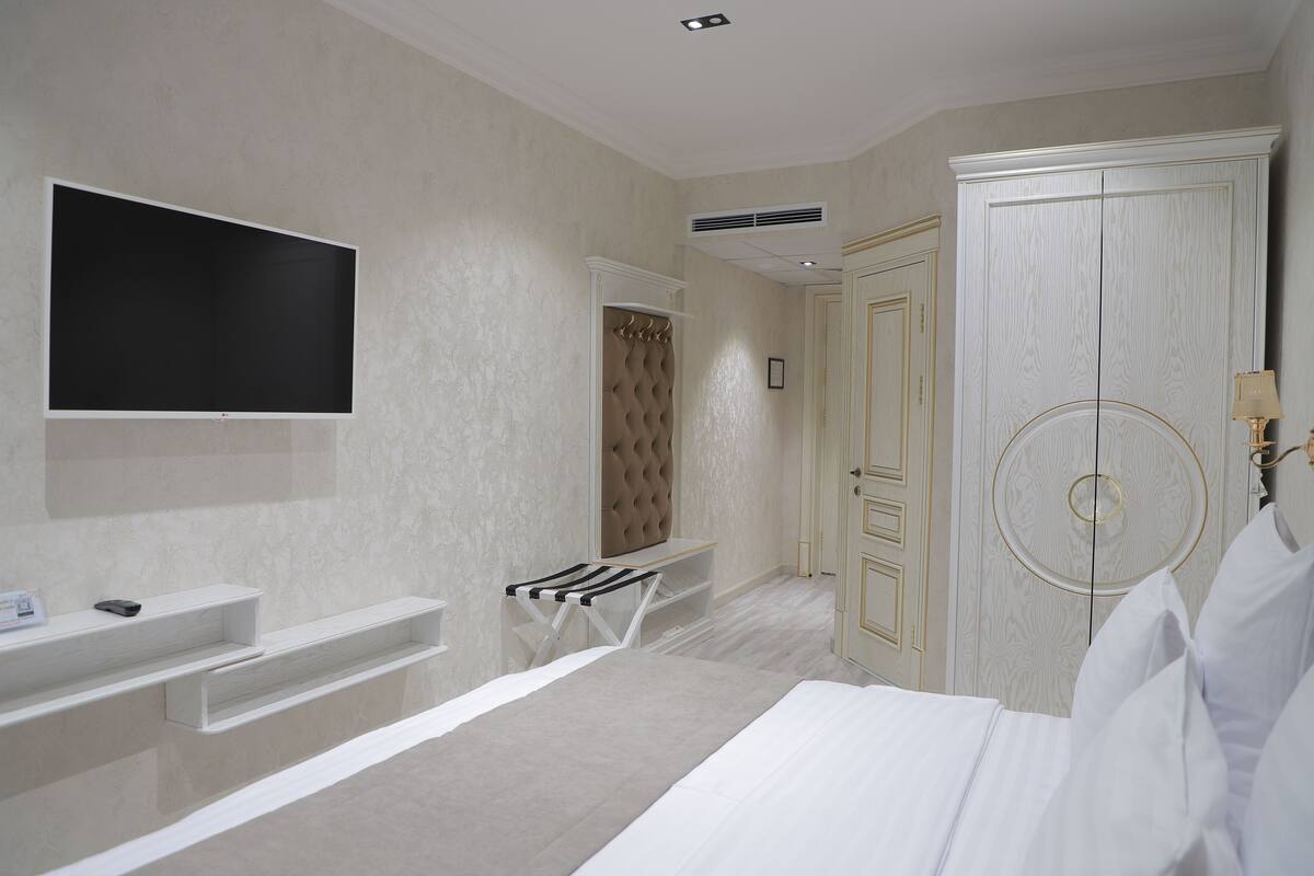 A bedroom with a bed, a TV mounted on the wall, a wardrobe, and a vanity with a mirror.