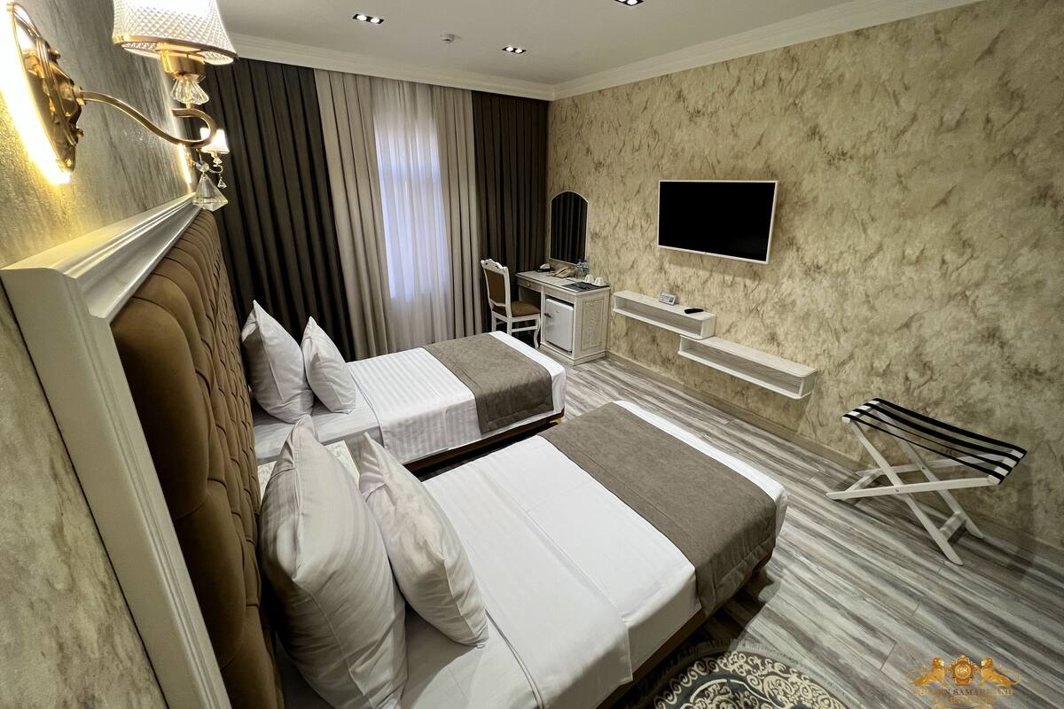 A hotel room with two beds, a desk, a TV, and a bathroom.