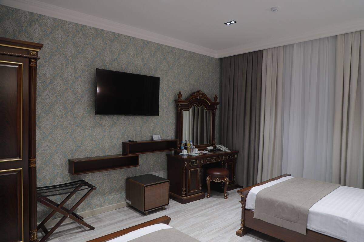 A hotel room with a bed, a desk, a chair, a television, and a wardrobe.