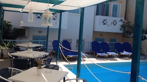 An outdoor pool area with lounge chairs, tables, and a covered seating area with hanging lanterns. - Renia Studios -Studio for 2 plus 1 pers  with a swimming pool (Agia Pelagia)