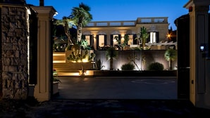 A gated entrance to a property with a stone wall, a paved driveway, and a well-lit building in the background. - Villa Callari 6 2 in San Felice Circeo (San Felice Circeo)