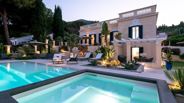 A poolside area with a pool, lounge chairs, and a building with a balcony.