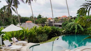 A pool area with lounge chairs and a hot tub, surrounded by tropical plants and palm trees. - Hot Stone Club Ubud (Sukawati)