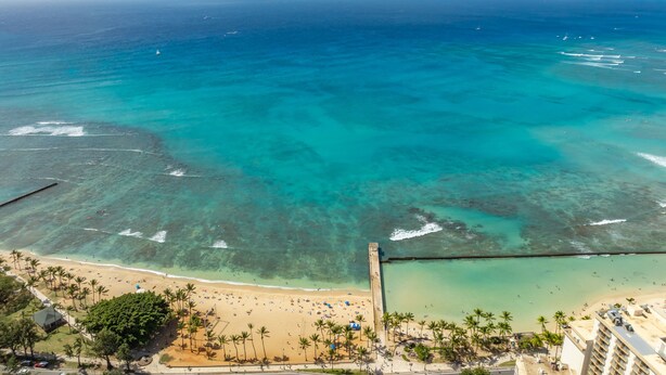 A beach with clear turquoise water, palm trees, and a pier. - Take-It-Easy Waikīkī Beach Condo (Honolulu)