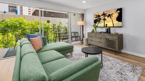 A modern living room with a green sofa, a small round table, and a painting of palm trees. - Take-It-Easy Waikīkī Beach Condo (Honolulu)