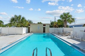 A swimming pool with clear blue water, surrounded by white lounge chairs and palm trees.
