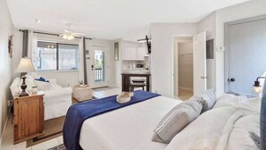 Ein Schlafzimmer mit einem Bett, einem Schreibtisch und einem Stuhl. Ein Fenster mit Jalousien und eine Tür zu einem anderen Raum.