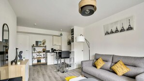 A modern living room with a grey sofa, yellow and white chairs, a coffee table, and a dining area with a white cabinet and a black chair. - Chic studio near Paris - La Defense (Bezons)