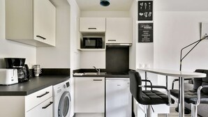 A compact kitchen with a washing machine, a microwave, and a coffee maker. There is a dining area with a table and chairs. - Chic studio near Paris - La Defense (Bezons)