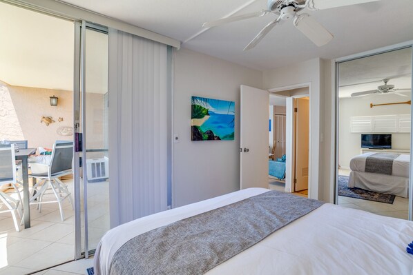 A hotel room with a bed, a painting, a desk with chairs, and a sliding door to a balcony.
